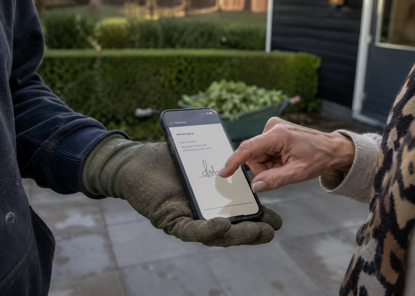 Een klant zet met haar vinger een handtekening op de telefoon die de hovenier vasthoudt